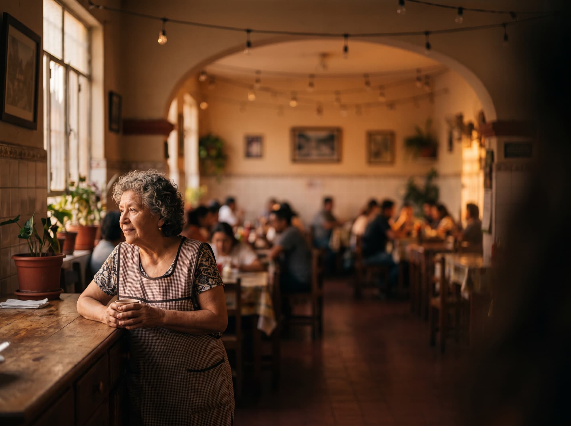 La dueña de un comedor de barrio apoyada en su mostrador con el salón lleno