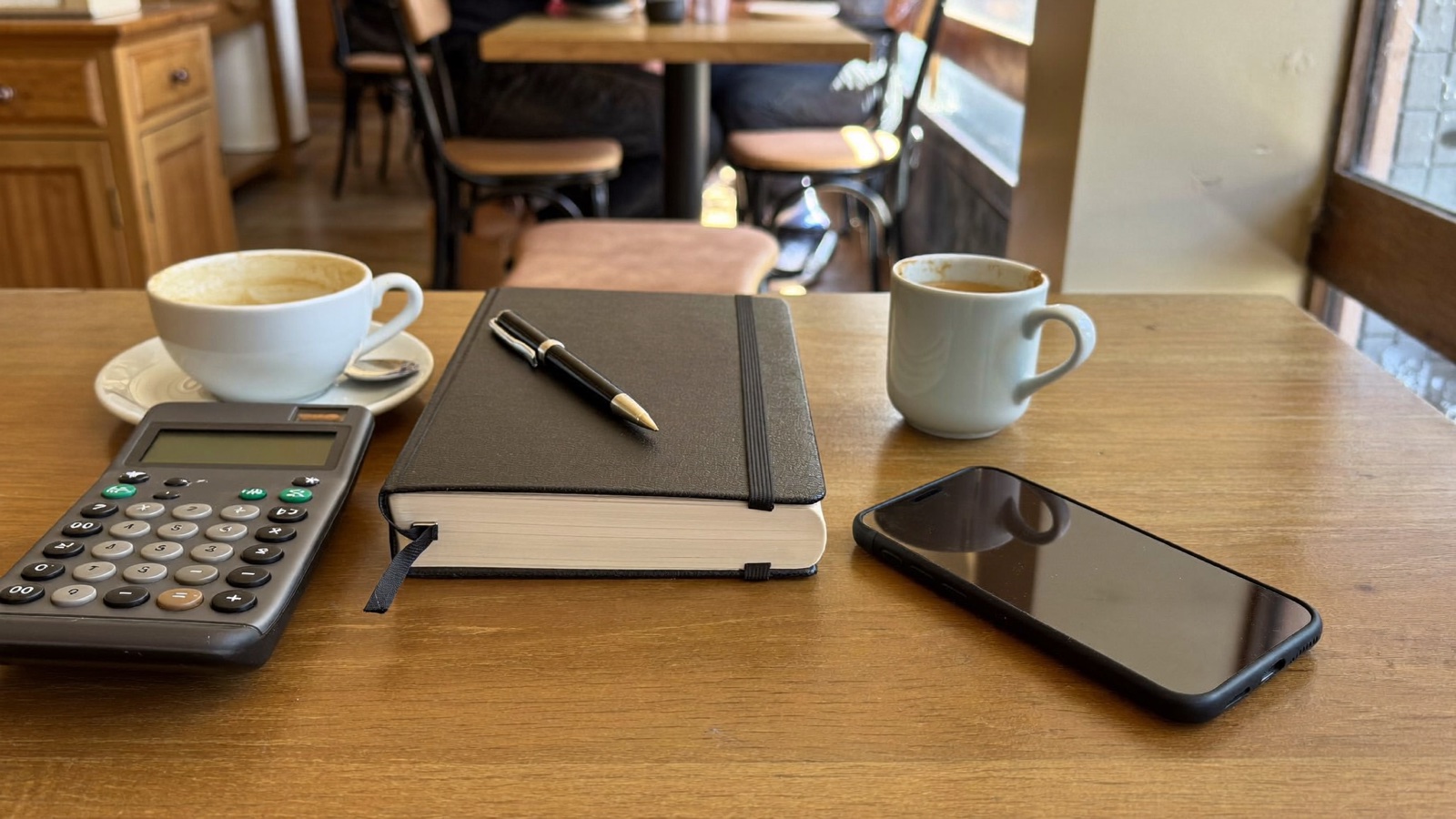 Las manos del dueño estudiando su cuaderno junto a un cortado